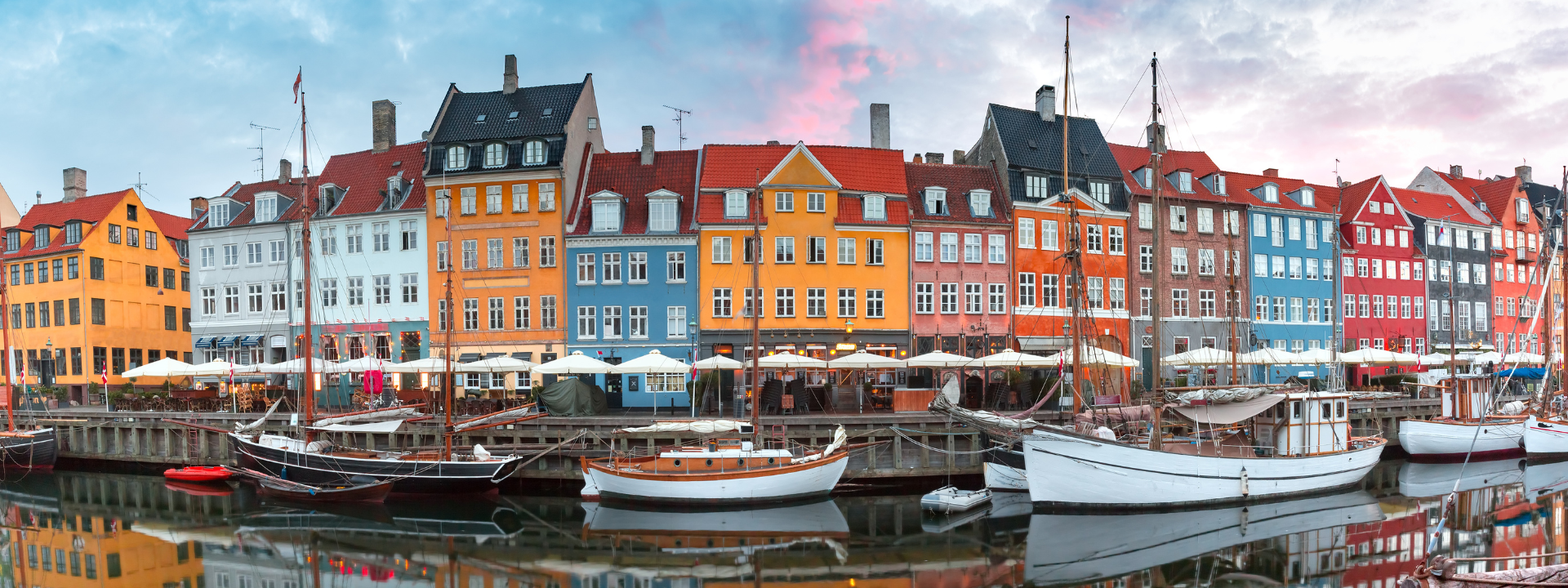 Colorful historic townhouses and sailboats along the Nyhavn canal in Copenhagen, reflected in the water.